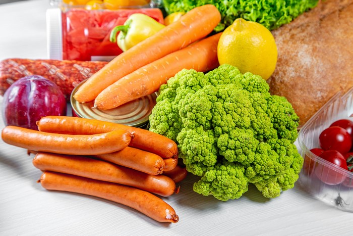Assortment of groceries including sausages, carrots, broccoli, lemon, bread, and tomatoes