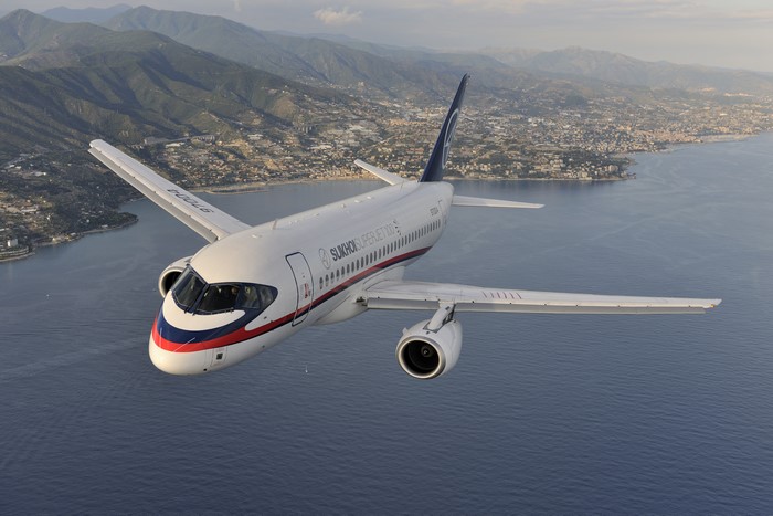 Sukhoi Superjet 100 flying over a coastal city