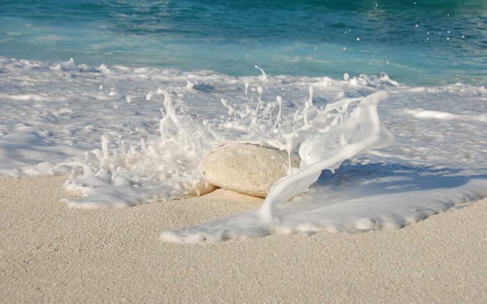 Wave splashing on a rock on a sandy beach