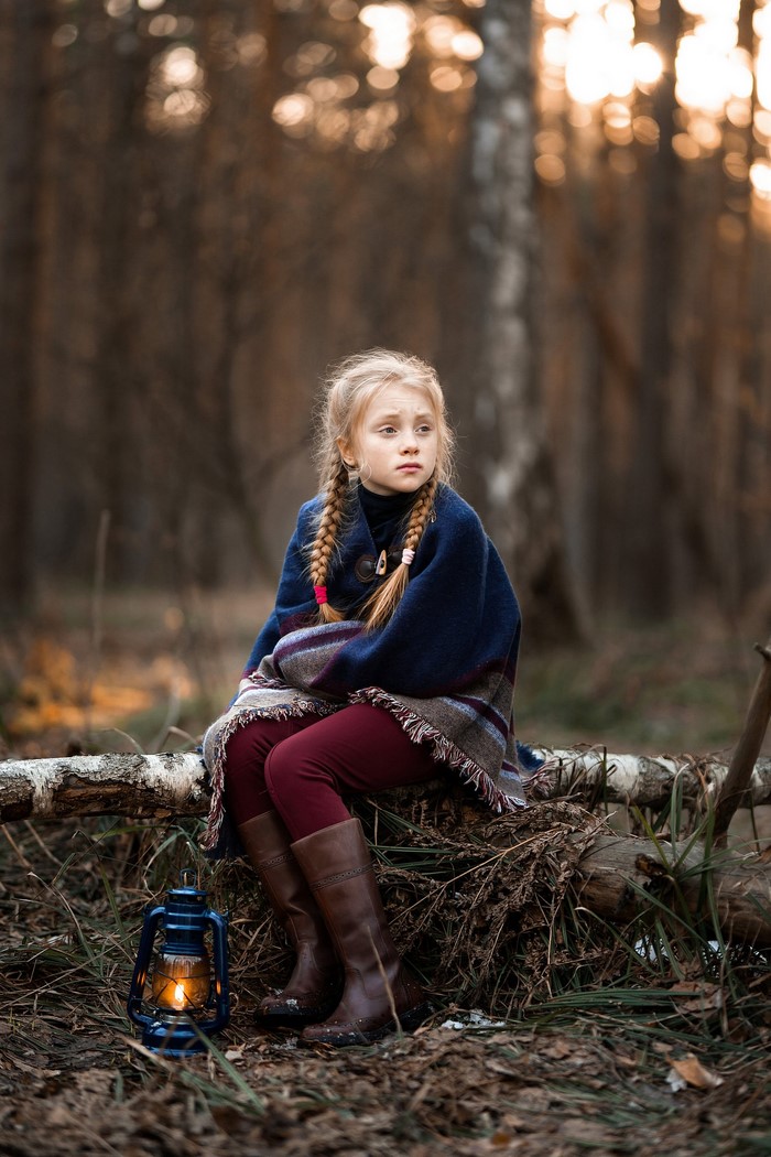 Girl with braided hair sitting in a forest with a lantern