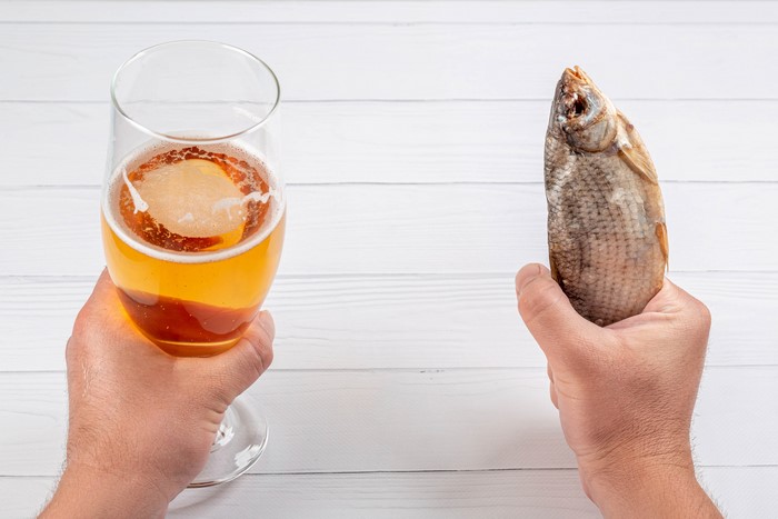 Hands holding beer and dried fish