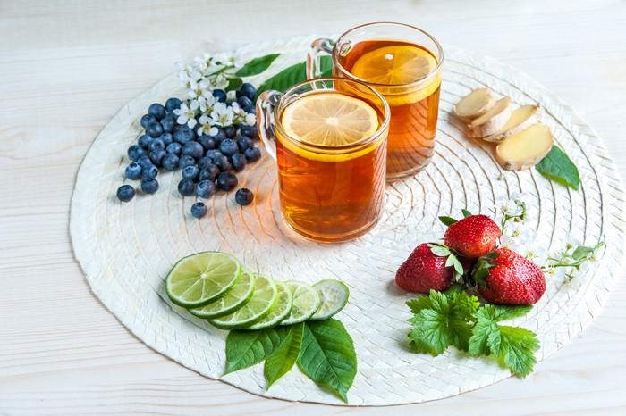 Two glasses of tea with lemon, blueberries, strawberries, lime, and ginger