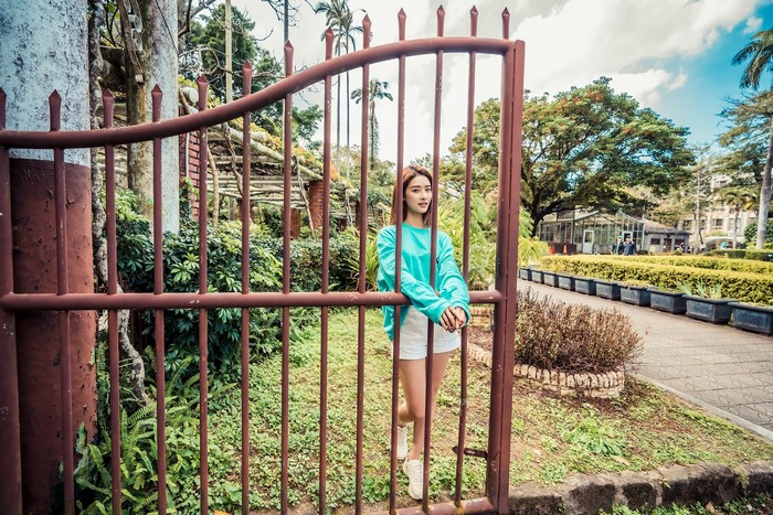 Asian woman in teal shirt and white shorts behind a gate