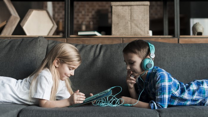 Two children using a tablet computer on a sofa