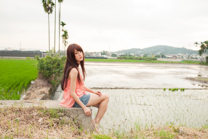 Asian woman with brown hair sitting by rice fields