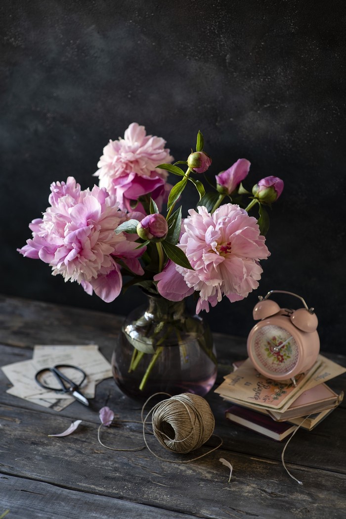Pink peonies in a vase with an alarm clock and scissors