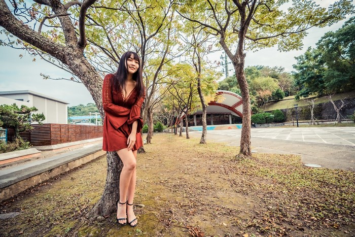 Asian woman in red dress posing by a tree
