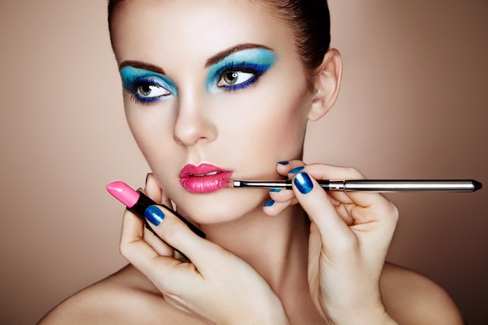 Woman applying pink lipstick with makeup brush
