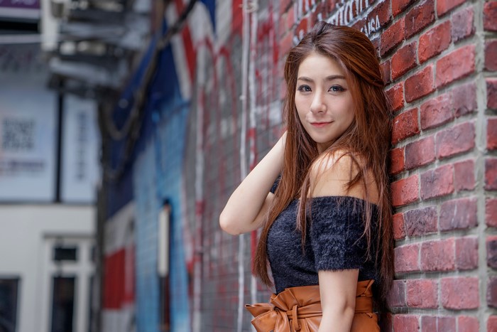 Asian woman with brown hair leaning against a brick wall