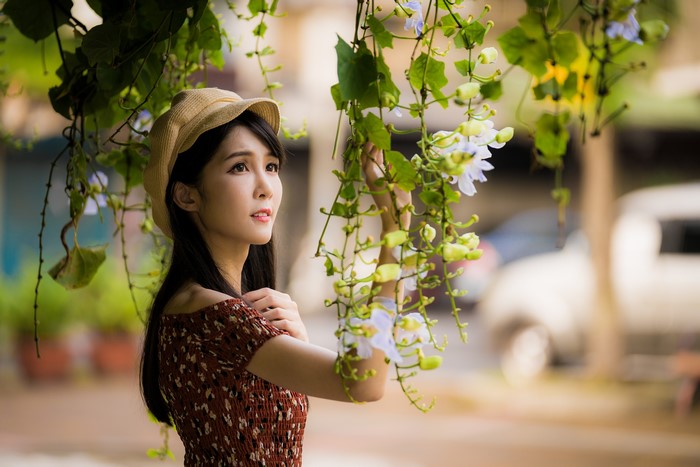 Asian woman in a dress and hat under branches