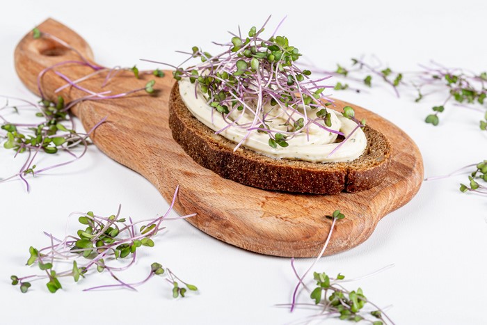 Bread with cream and sprouts on cutting board