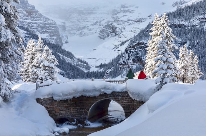 Snowy bridge over stream with mountains and trees in Banff