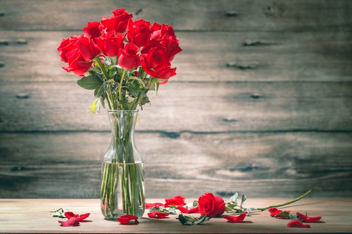 Bouquet of red roses in a vase on a table with petals