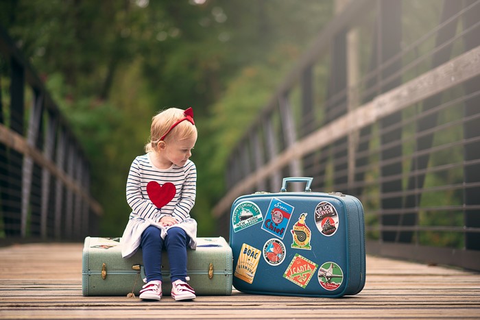 Little girl sitting on suitcase on a bridge