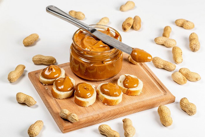Peanut butter on bread slices with peanuts and knife