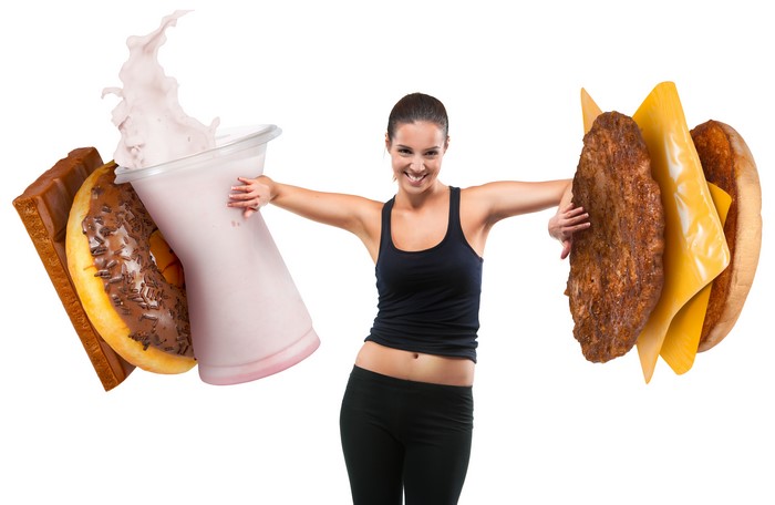 Woman holding a hamburger and a milkshake with donuts and chocolate