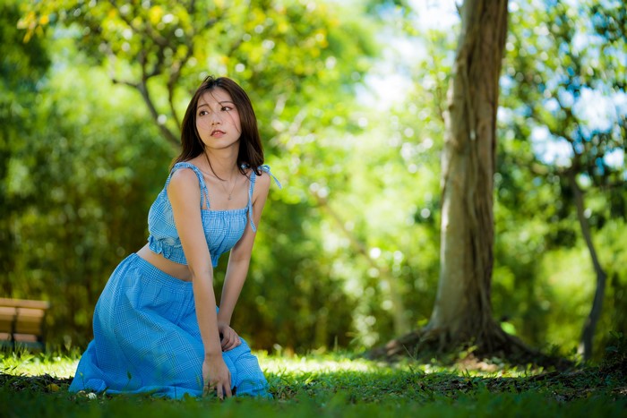 Asian Woman in Blue Plaid Outfit Kneeling in Park