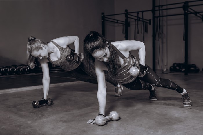 Two women doing dumbbell plank exercise in gym