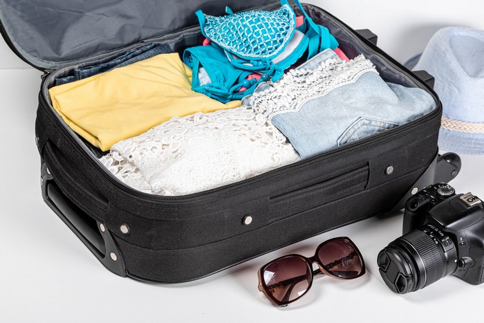 Suitcase packed with clothes, camera, sunglasses, and hat