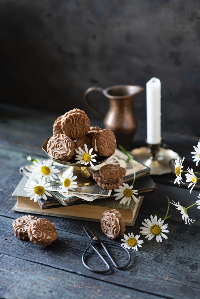 Chocolate cookies with cream and daisies on a wooden table