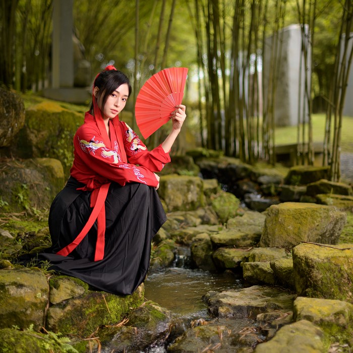 Asian woman in kimono holding a hand fan by a stream