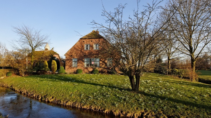 Brick farmhouse with thatched roof by a canal