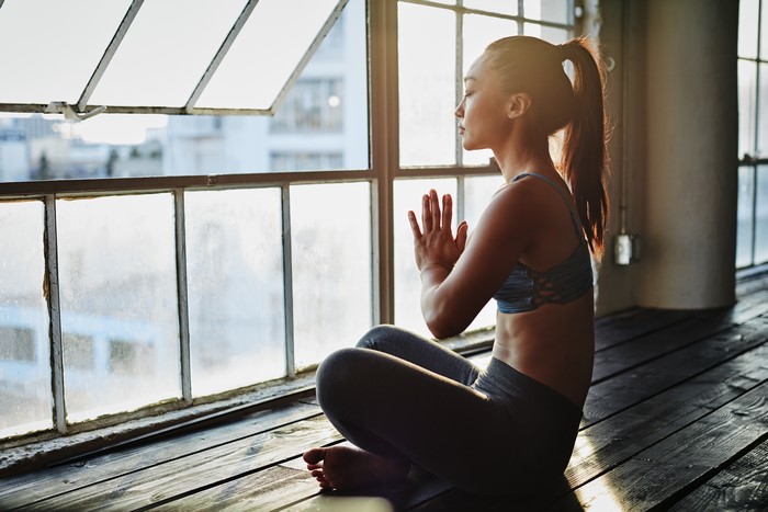 Asian woman meditating in yoga pose by window