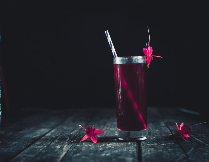 Glass of red juice with flowers on wood