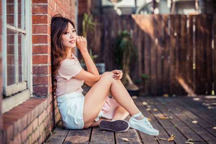 Asian woman with brown hair sitting by a brick wall