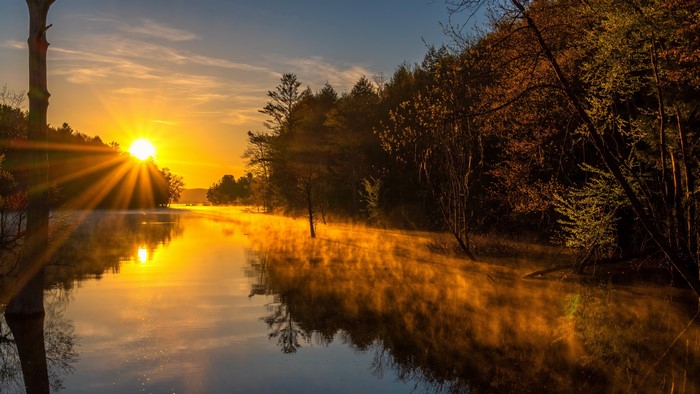 Sunrise over a misty river with sun rays