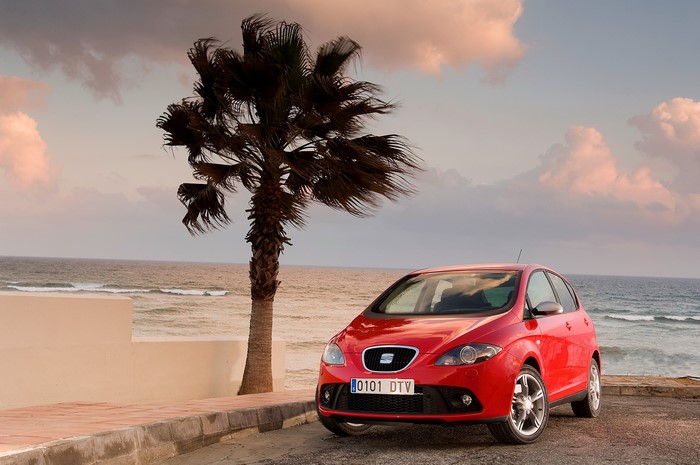 Red Seat car parked by the ocean with palm tree