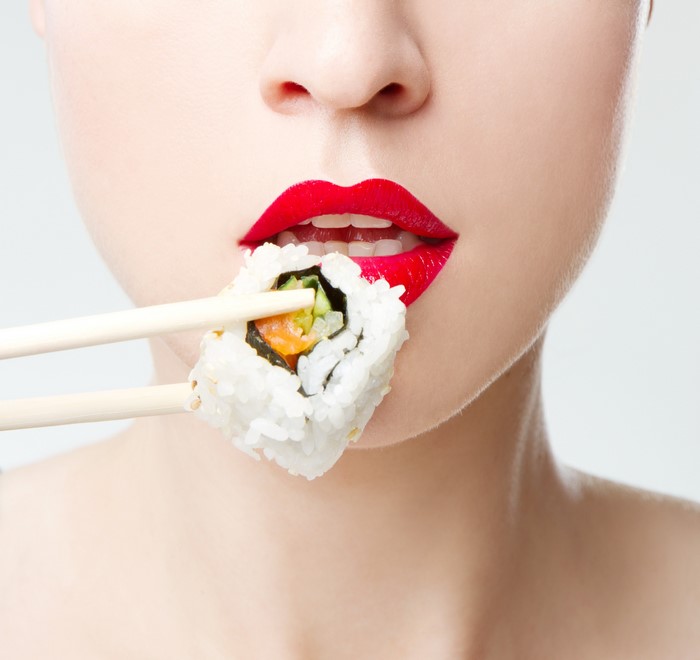 Woman with red lips eating sushi with chopsticks
