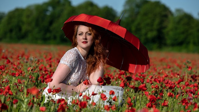 Redhead woman with red umbrella in poppy field