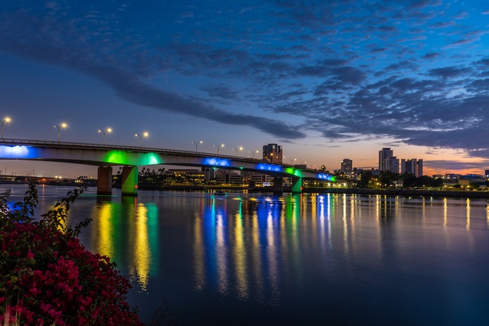 Bridge illuminated with blue and green lights over a river at dusk in Long Beach, California
