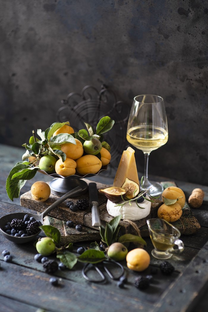 Wine, cheese, apricots, figs, and berries on wooden planks