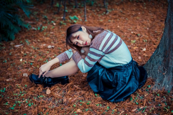 Asian woman sitting on the ground in a sweater and skirt