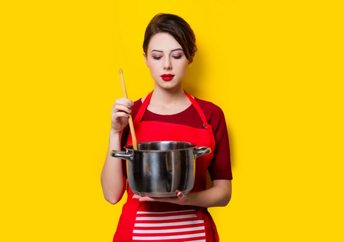 Woman in apron cooking with saucepan and wooden spoon