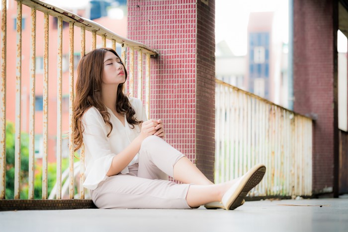 Asian woman with brown hair sitting by a fence