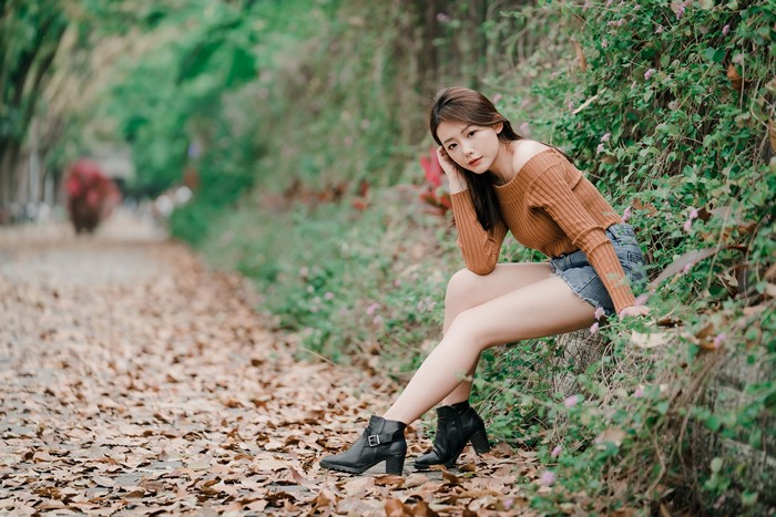 Asian woman with brown hair sitting on a path covered in leaves