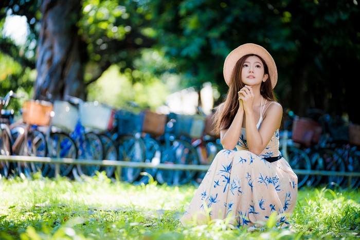 Asian woman in dress and hat sitting on grass