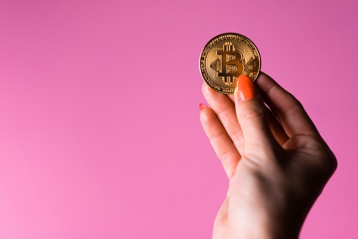 Hand holding a Bitcoin coin on a pink background