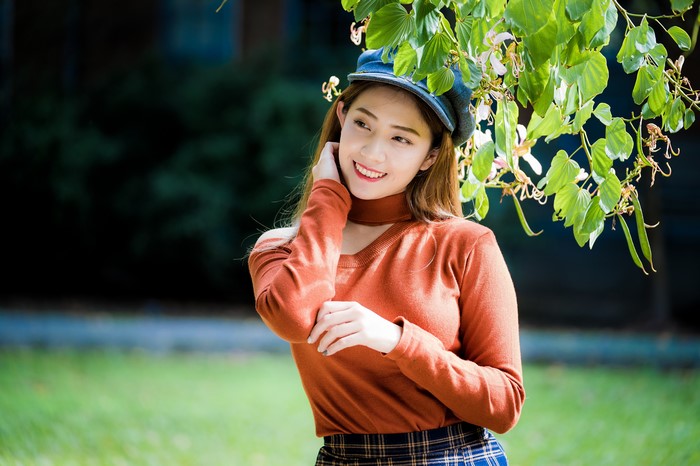 Asian woman wearing a baseball cap and orange sweater
