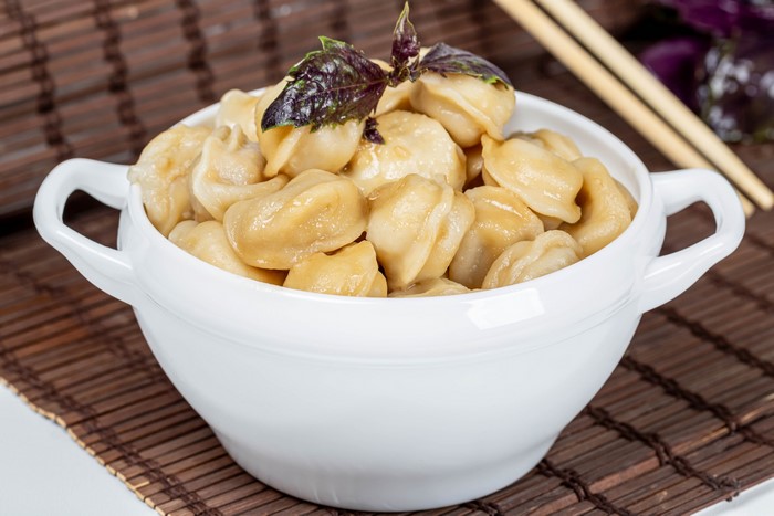 Pelmeni in a white bowl with basil