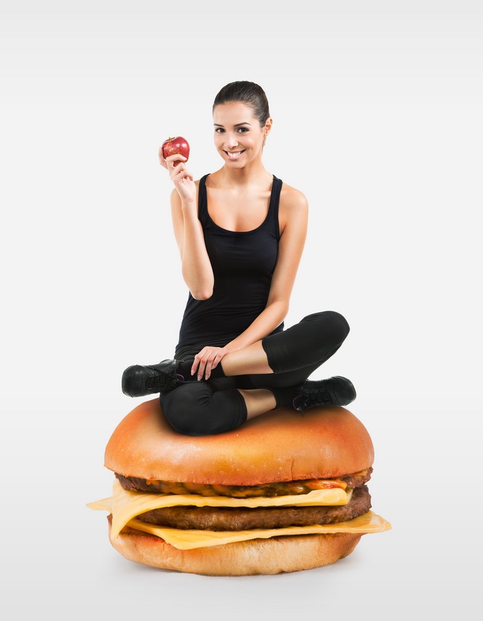 Woman sitting on a hamburger holding an apple