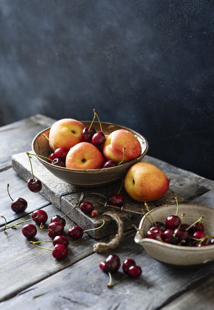 Peaches and cherries in bowls on wooden planks