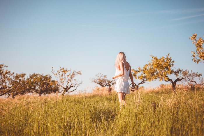 Blonde girl in white dress strolling in a grassy field