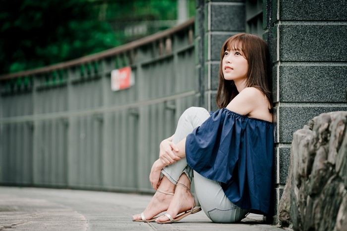 Asian woman with brown hair sitting by a wall