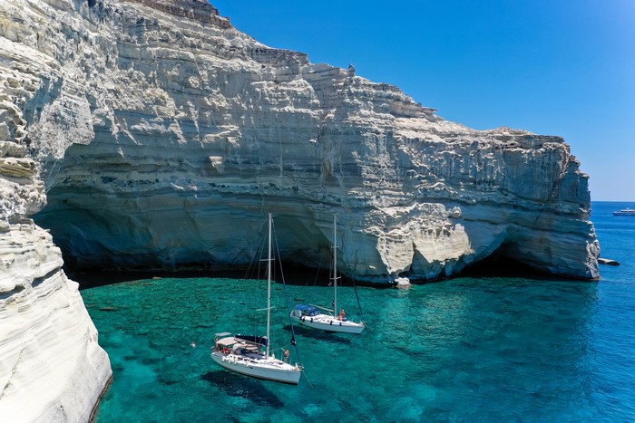 Sailboats in a turquoise bay near white cliffs in Milos, Greece