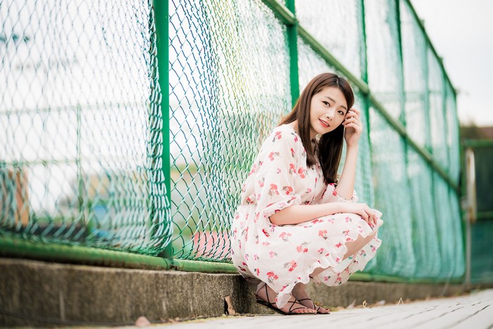 Asian woman in floral dress by fence