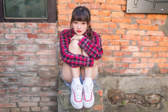 Asian girl in plaid shirt sitting by brick wall